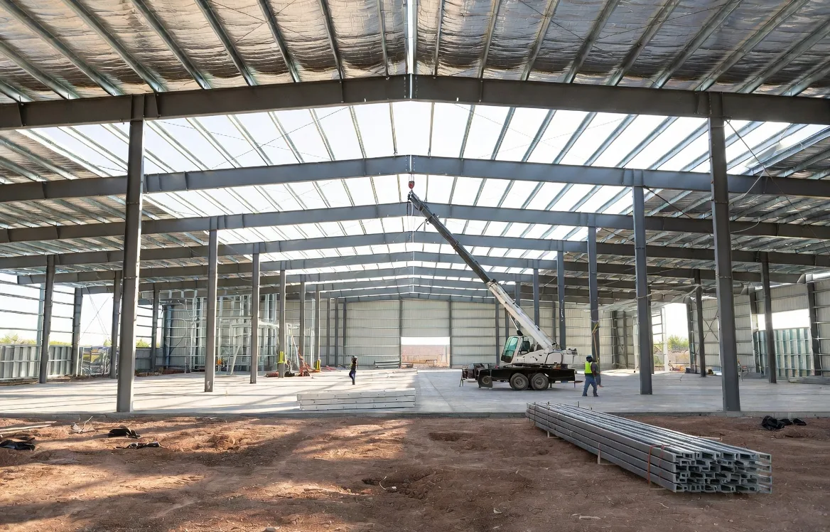 Prefabricated steel warehouse under erection in northern Mexico, mobile crane positioning a rafter